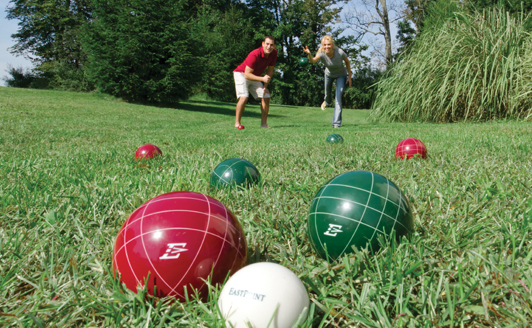 2 people playing bocce ball in a grassed area 2 green balls 3 red balls one white ball basic equipment bocce ball bocce ball set with different colored balls